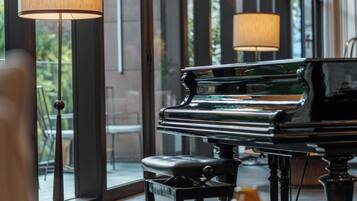 A grand piano in a well-lit room with large windows and floor lamps.