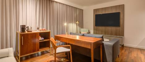 Une chambre d’hôtel moderne avec une table à manger en bois, un canapé, un téléviseur fixé au mur et un minibar.