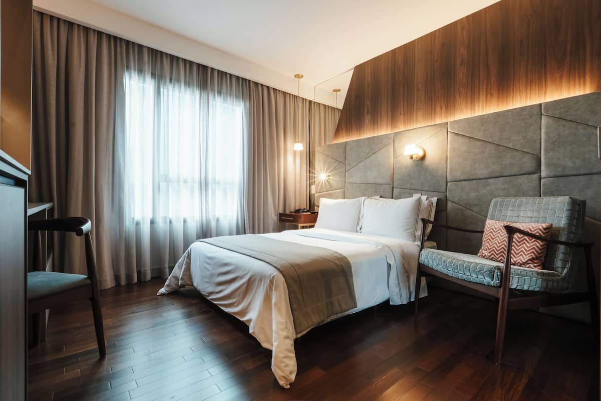 Una habitación de hotel moderna con una cama grande, un cabecero de madera, un área de descanso con una silla y un escritorio.