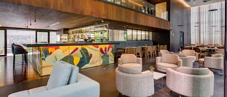 Un lobby moderno con zona de bar, espacios de asiento y un alto techo con luz natural.