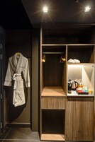 Un bagno moderno con un accappatoio appeso al muro, un mobile bagno in legno con un bollitore e articoli da toilette, e uno scaffale con scarpe.