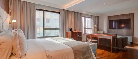 A modern hotel room with a large bed, a desk, and a TV.