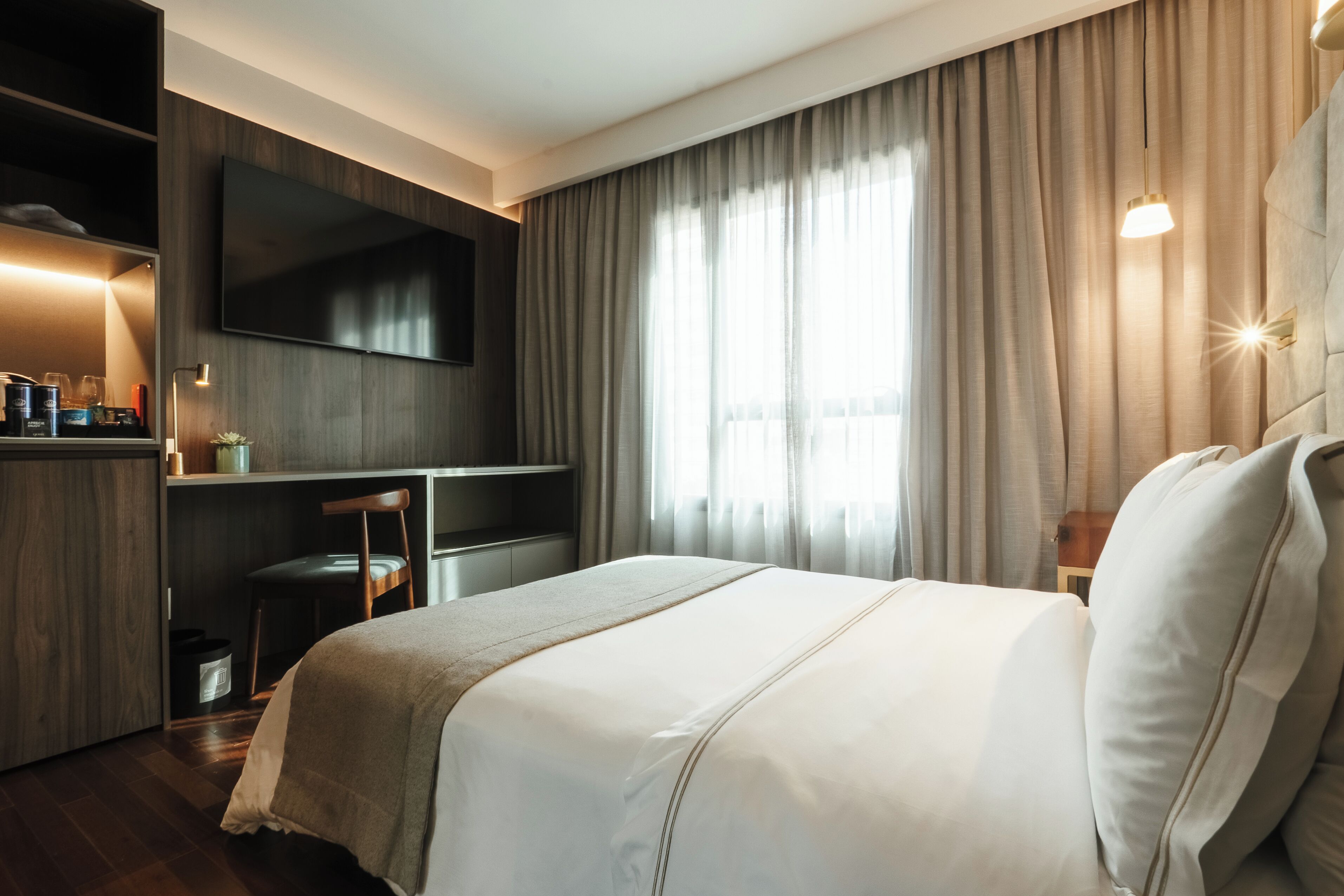 Habitación de hotel con cama, escritorio, televisión y ventana con cortinas.