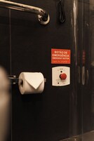 A bathroom with a toilet paper roll, a handrail, and an emergency button.