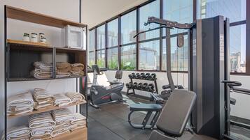A gym with exercise equipment, towels, and a view of the city through large windows.