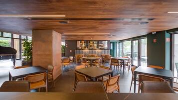 Un restaurante moderno con techo de madera, ventanas amplias y un piano. Mesas y sillas dispuestas para comer.