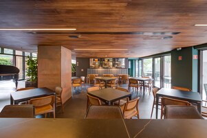 Un restaurante moderno con techo de madera, ventanas amplias y un piano. Mesas y sillas dispuestas para comer.