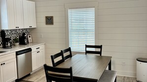 Una cocina moderna con armarios blancos, una mesa de comedor con sillas, un ventilador de techo y una ventana con persianas.