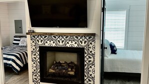 Un salón con chimenea, un televisor de pantalla plana colocado encima y una cama con ropa de cama a rayas.