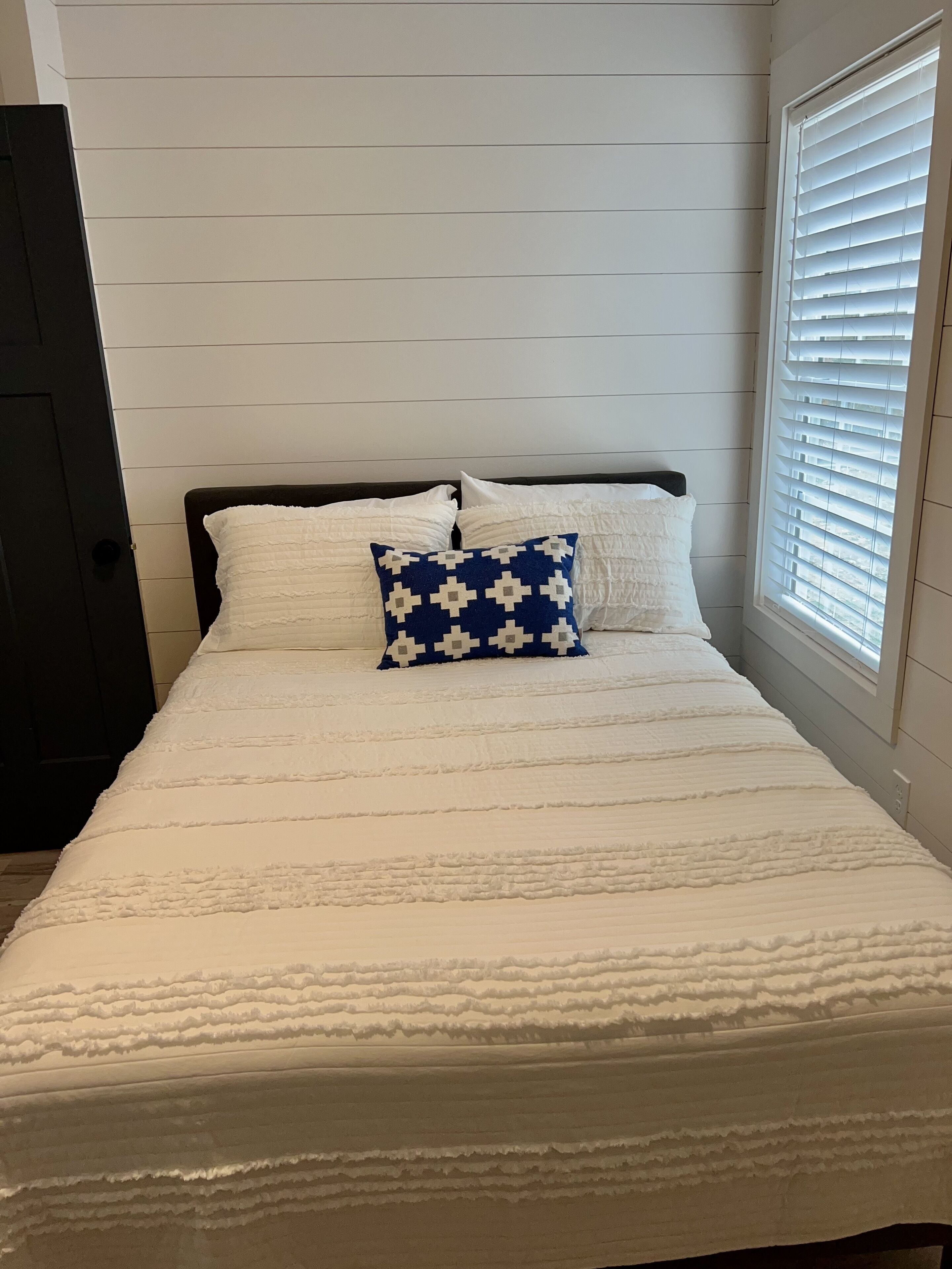A neatly made bed with a white duvet and a single blue patterned pillow.