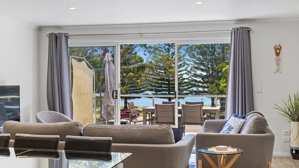 A modern living room with a glass door leading to a balcony overlooking a body of water and trees.