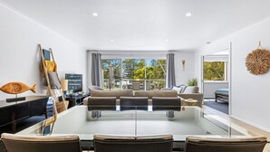 A modern living room with a glass dining table, sofas, and a TV.