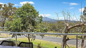 A balcony with a view of a road, trees, and a mountain in the distance. - Beautiful renovated Boardwalk Apartments Unit Eleven (Narooma)