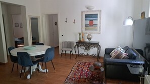 Ein Wohnzimmer mit Esstisch, Stühlen, einer Couch, einem Fernseher und einem Bild an der Wand.