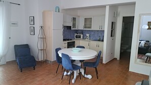 A compact kitchen with white cabinets, a round dining table with blue chairs, and a blue sofa in the living area. -  Beautiful hillside holiday rental with sea views and pool (Nuoro)