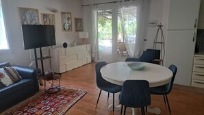 A living room with a sofa, a TV, a dining table with chairs, a kitchen area, and a sliding glass door leading to an outdoor space. -  Beautiful hillside holiday rental with sea views and pool (Nuoro)