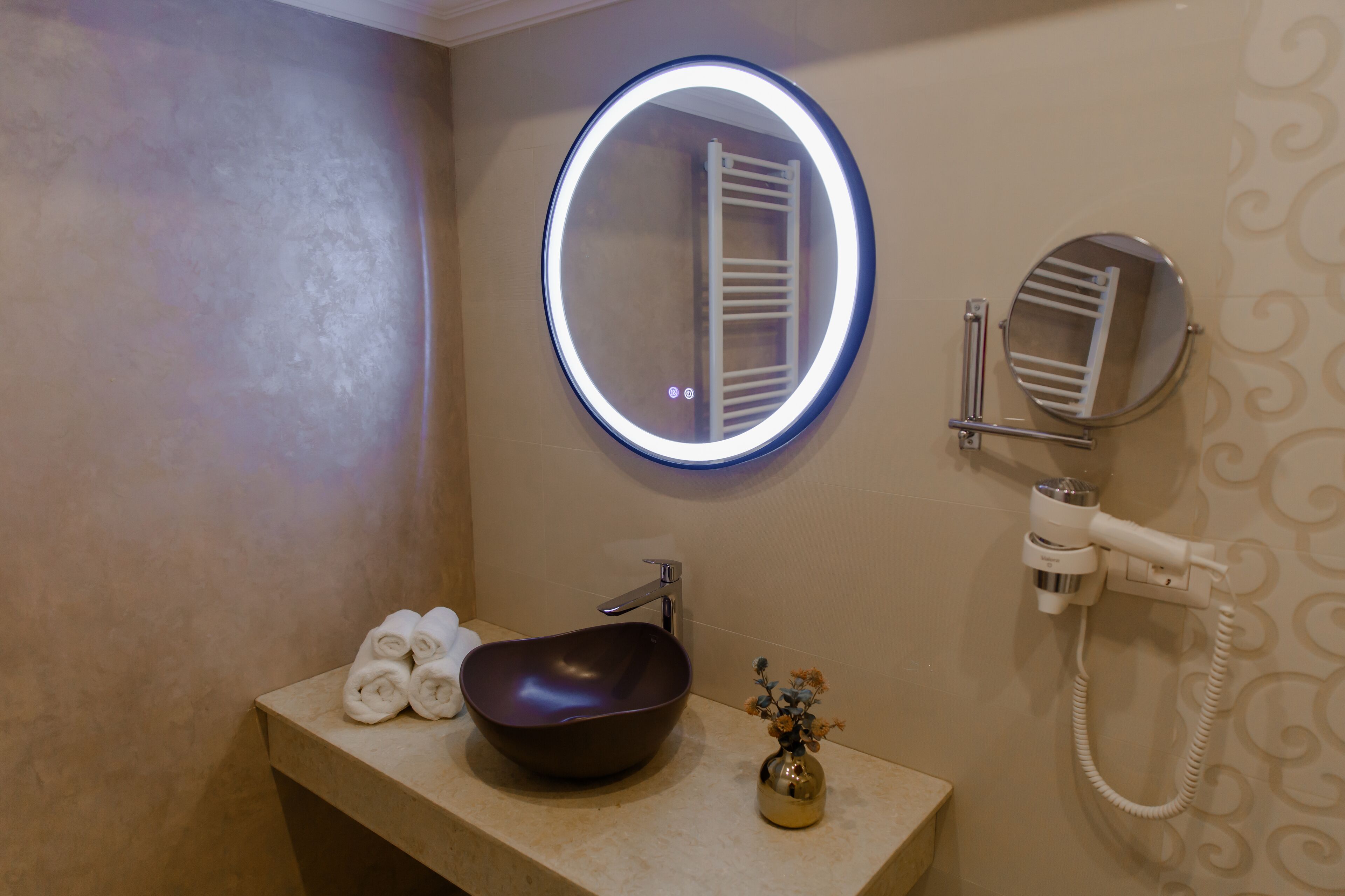A bathroom with a round mirror, a sink, a towel rack, and a hairdryer.