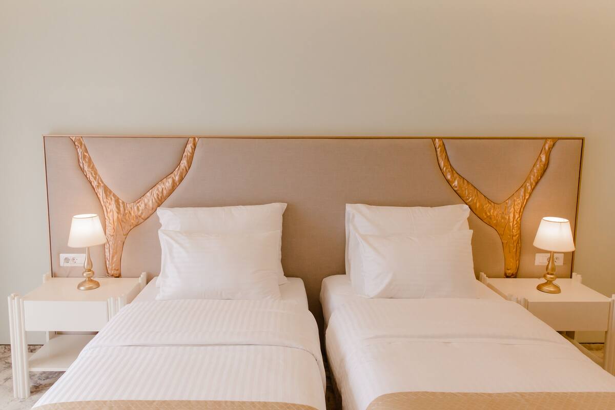 Ein Hotelzimmer mit zwei Betten, weißer Bettwäsche und einem großen, dekorativen Kopfteil.