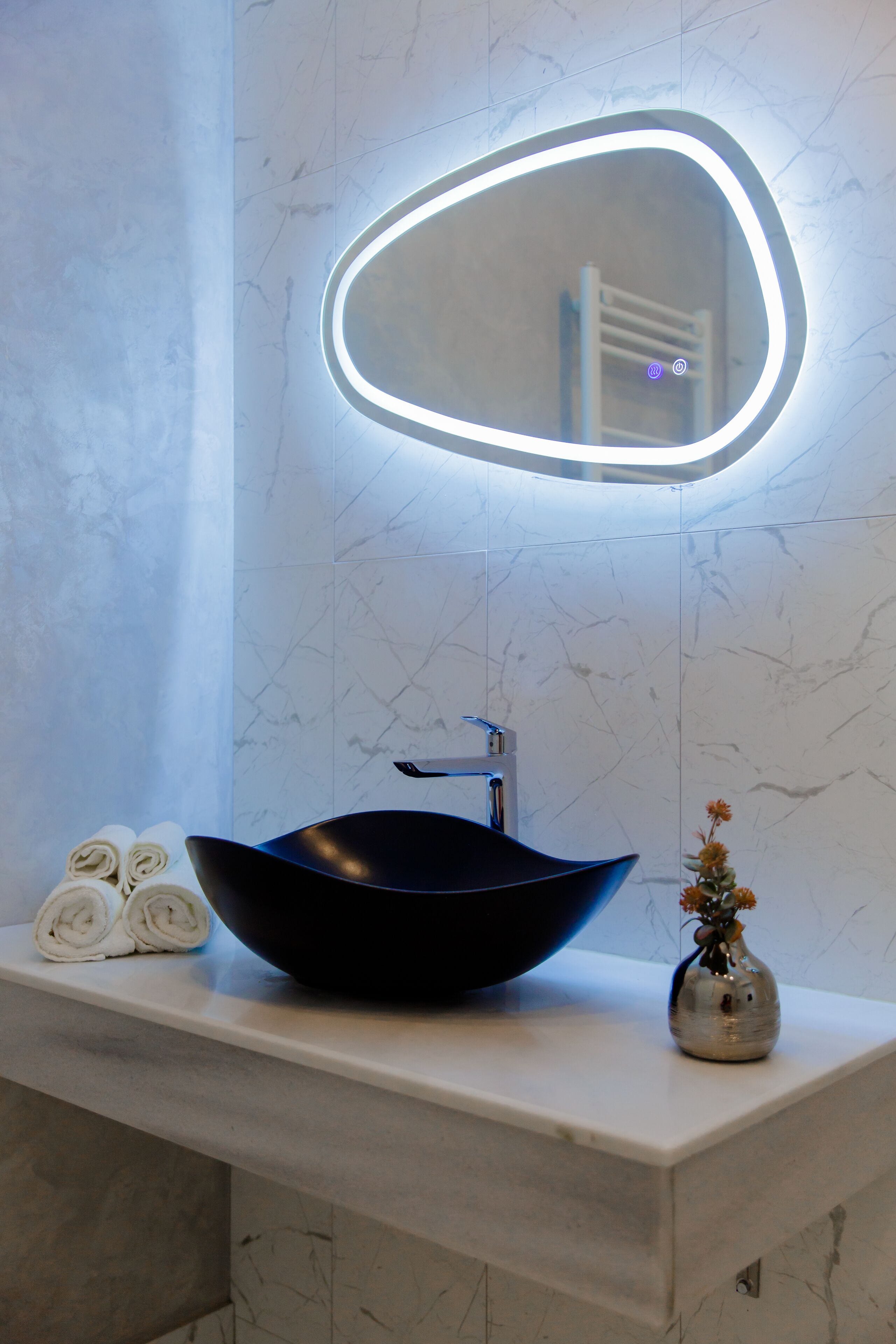 A bathroom with a black vessel sink, a mirror with a light, and a vase with flowers on the counter.