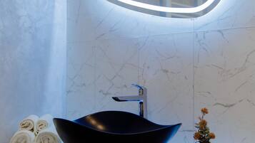 A bathroom with a black vessel sink, a mirror with a light, and a vase with flowers on the counter.