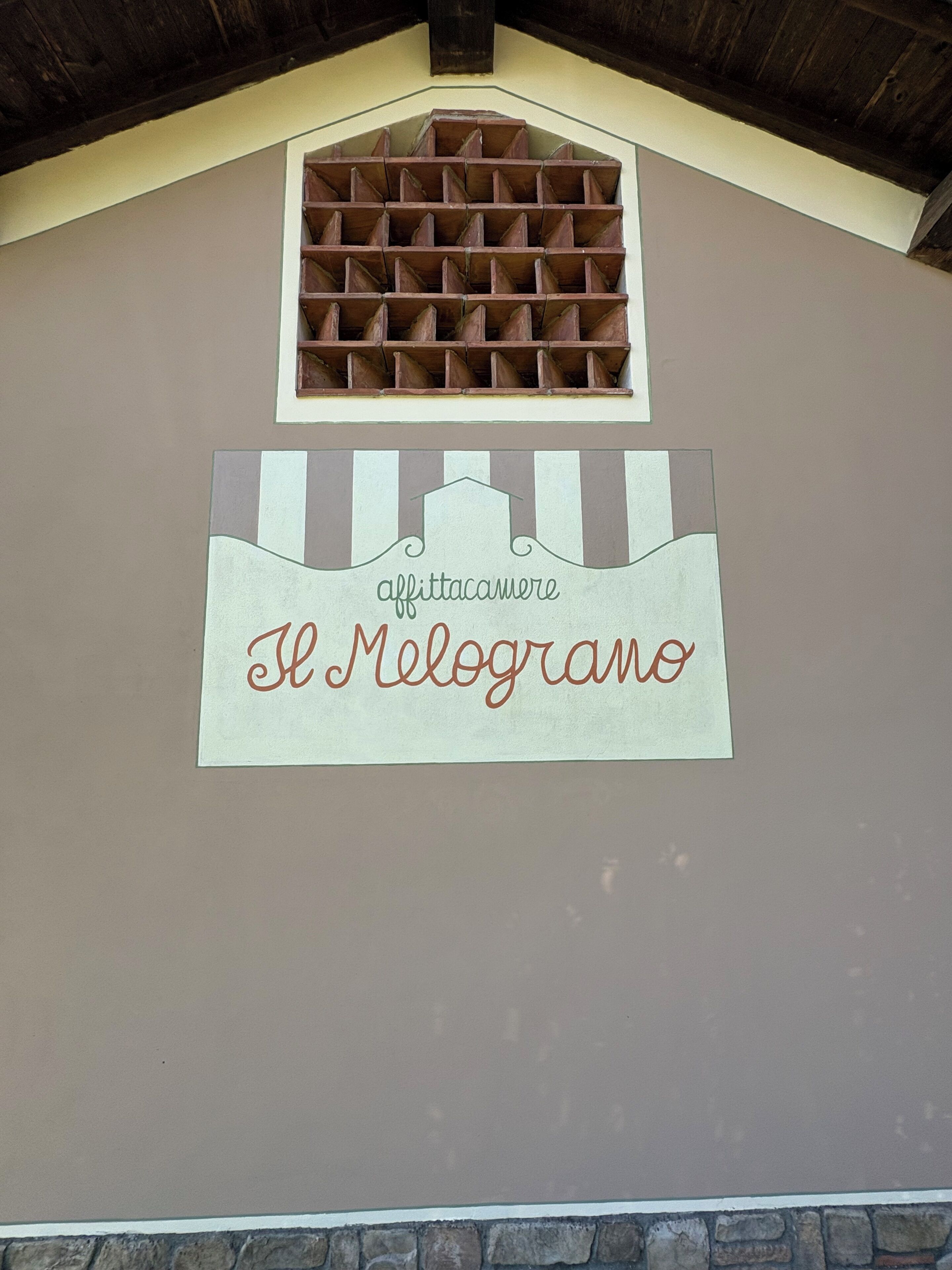A wall with a brown and beige color scheme, a window with a grid pattern, and a sign with 'affittacamere Il Melograno' written on it.