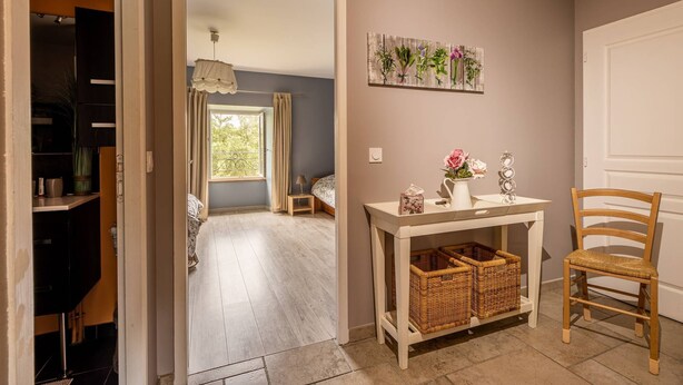 A room with a wooden floor, a white console table with baskets, a wicker chair, a bed with a headboard, and a wall-mounted plant display.