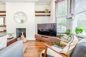 Una sala de estar con televisión, muebles de madera, chimenea y ventanas grandes con persianas.