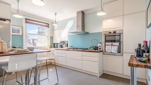 Ett modernt kök med vita skåp, en gasspis, en ugn och barstolar.