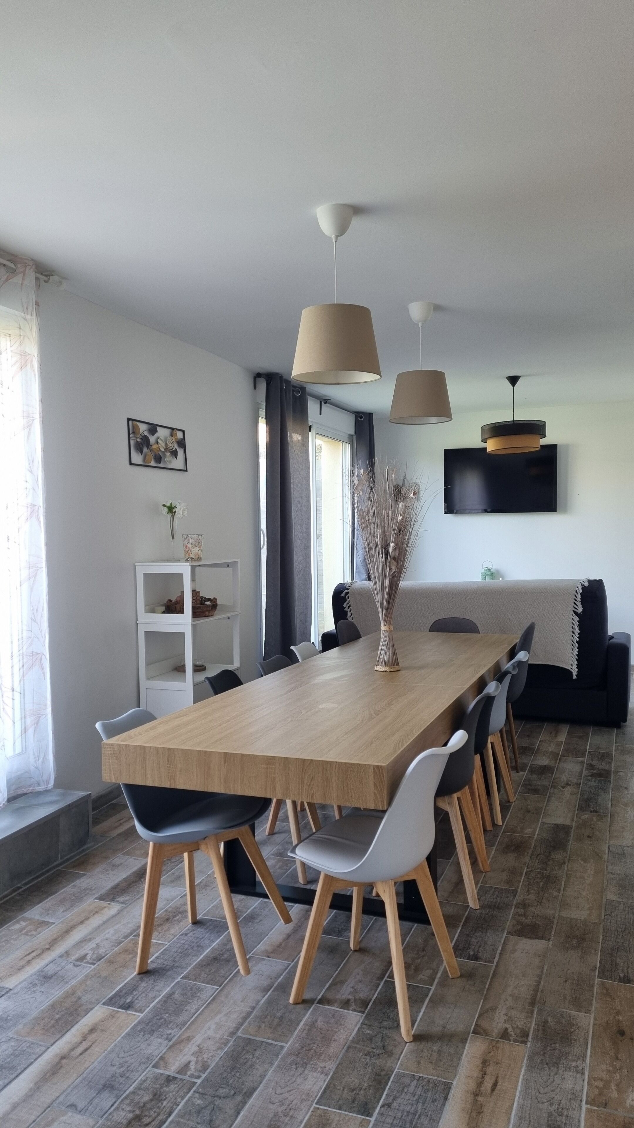 A modern dining area with a wooden table, black and white chairs, and pendant lighting.