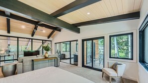 Een moderne slaapkamer met een groot bed, een bureau en een zithoek. Er zijn grote ramen en uitzicht op groen buiten.