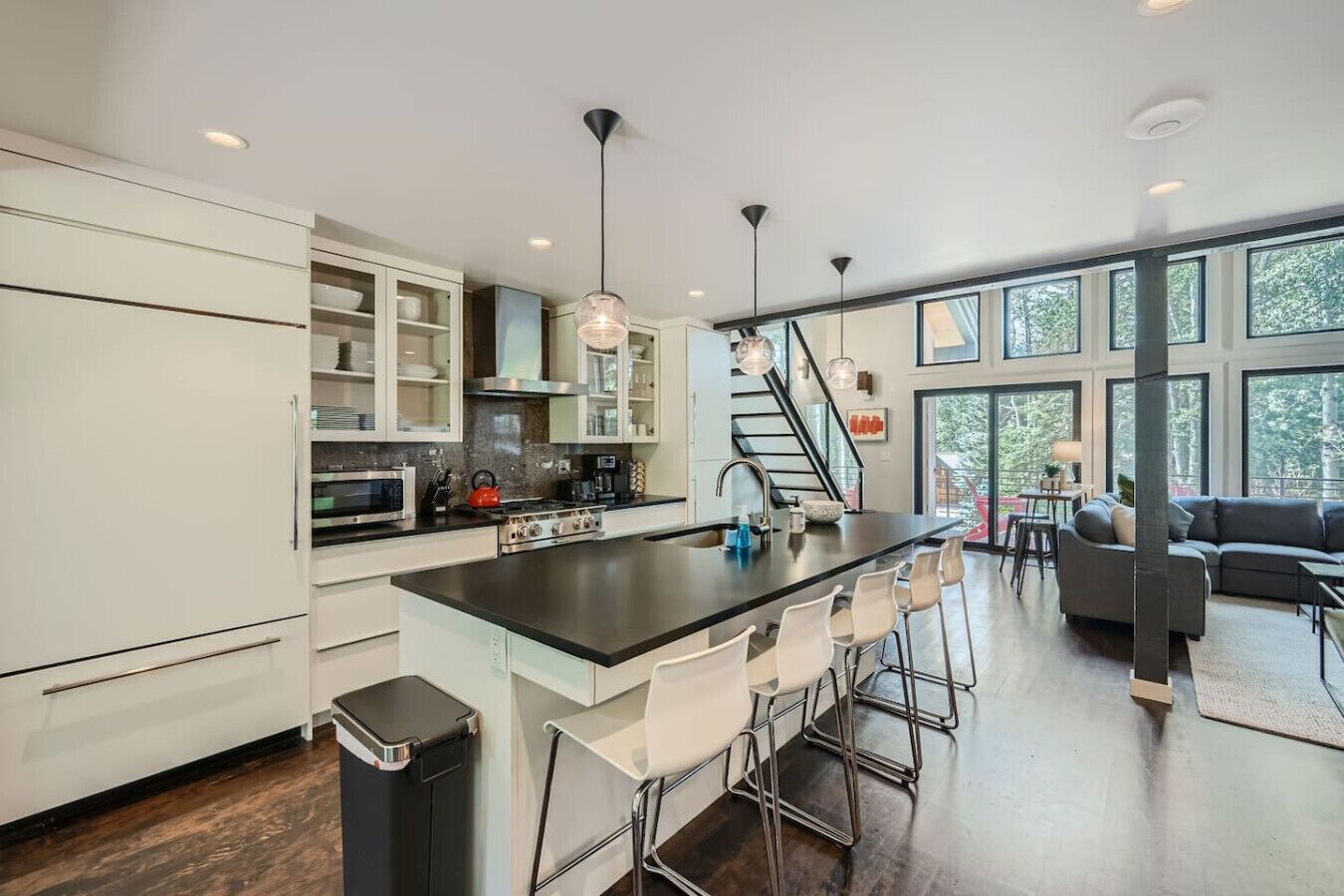 A modern kitchen with a central island, white cabinetry, stainless steel appliances, and a large window overlooking a deck.