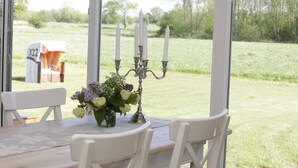 Uma área de refeições ao ar livre coberta, com uma mesa posta para dois, um candelabro com velas e vista para um campo gramado.