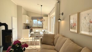Uma sala de estar aconchegante com um sofá bege, um espaço de jantar com mesa e cadeiras, uma cozinha com armários brancos e uma lareira.
