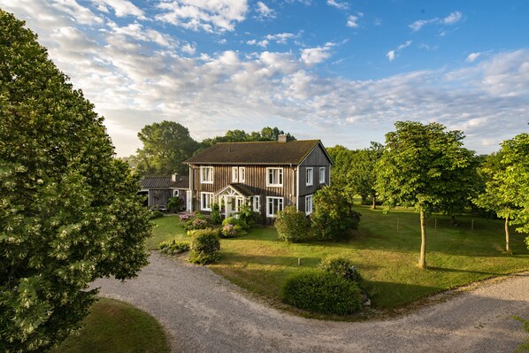 Ein zweistöckiges Haus mit Veranda, umgeben von einem gepflegten Rasen und Bäumen.