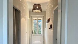Um corredor com piso estampado, uma porta branca com painéis de vidro e um lustre.