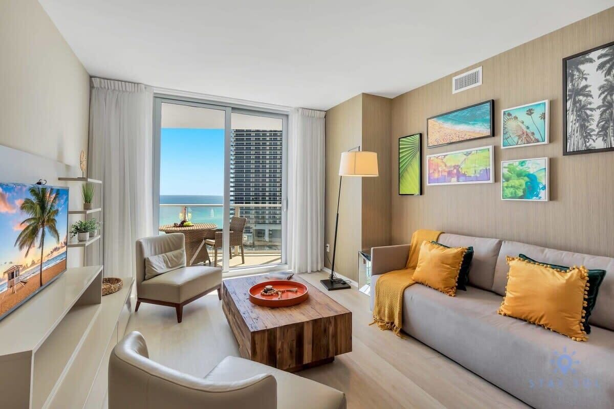 Quarto de hotel moderno com varanda, sofá, mesinha de centro e obras de arte nas paredes.