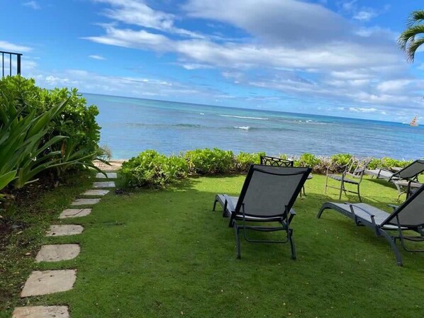 A grassy area with a stone path leading to a seating area with chairs facing a view of the ocean.