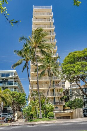 A multi-story hotel with balconies, surrounded by palm trees and other greenery.