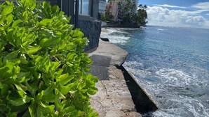 A coastal hotel with a stone pathway leading to the ocean, a view of the sea, and a building with large windows.