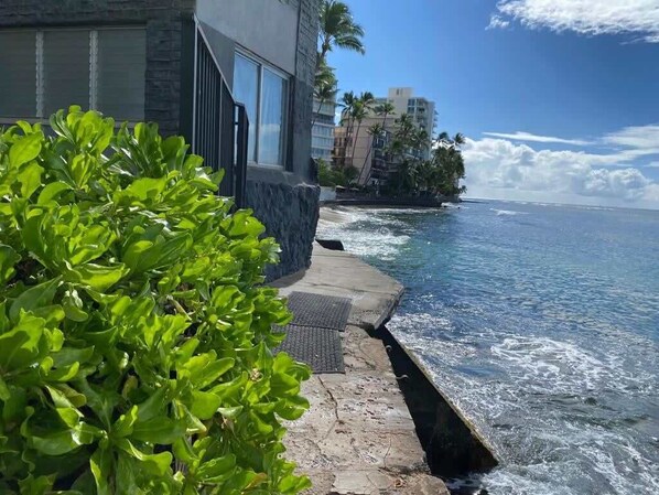 A coastal hotel with a stone pathway leading to the ocean, a view of the sea, and a building with large windows.