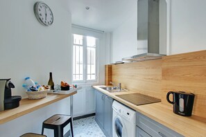 Una cocina compacta con lavadora, cafetera y lavabo.