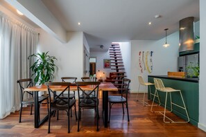 A modern dining area with a wooden table and chairs, a staircase, and a kitchen area with a green accent wall. - w* | Charming 2BR in Casco Antiguo (Panamá)