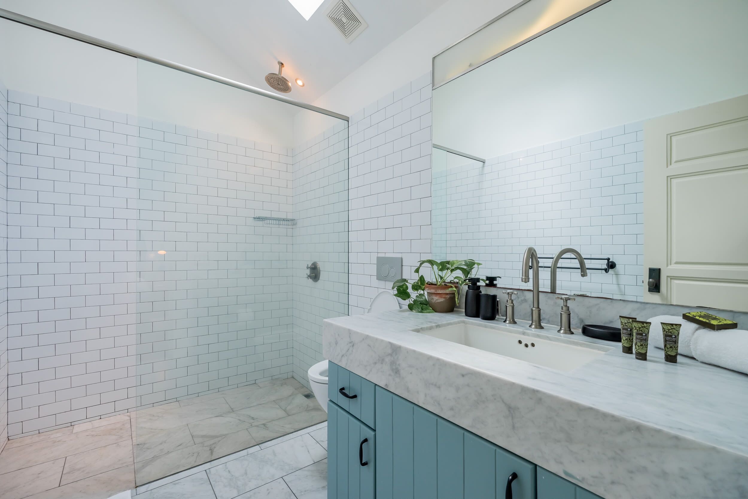 A modern bathroom with white subway tiles, a marble countertop, a large mirror, and a shower area.