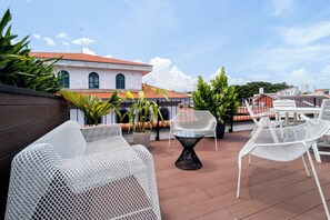A rooftop terrace with white wicker furniture, potted plants, and a view of a building with a red-tiled roof. - w* | Refined 2BR in Casco Viejo (Panamá)