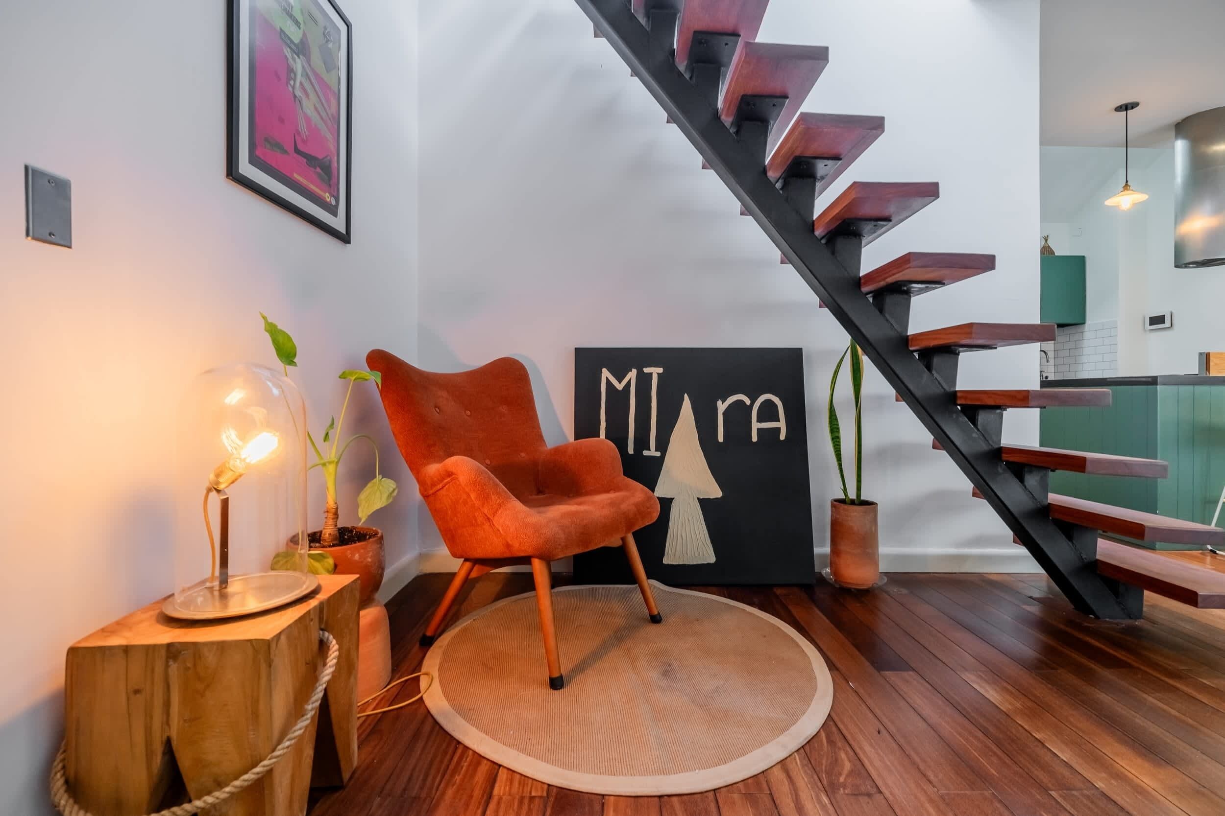 A modern interior with a wooden staircase, a red chair, a round rug, and a wall with a geometric design.