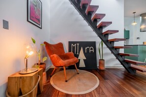 Een modern interieur met een houten trap, een rode stoel, een rond tapijt en een muur met een geometrisch ontwerp.