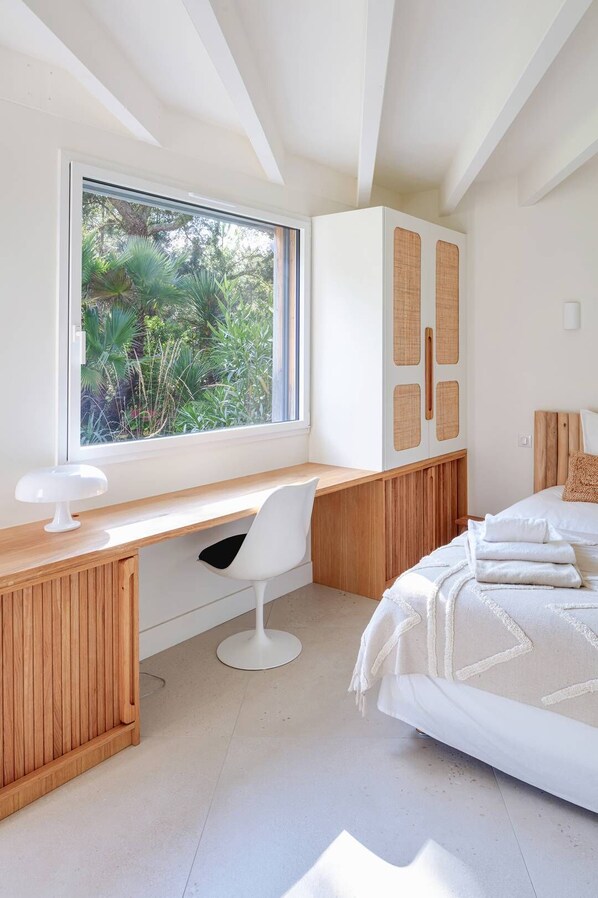 A bedroom with a wooden desk, a white chair, a bed with white bedding, and a window with a view of greenery. - BEAUTIFUL VILLA IN CAPBRETON (CAPBRETON)