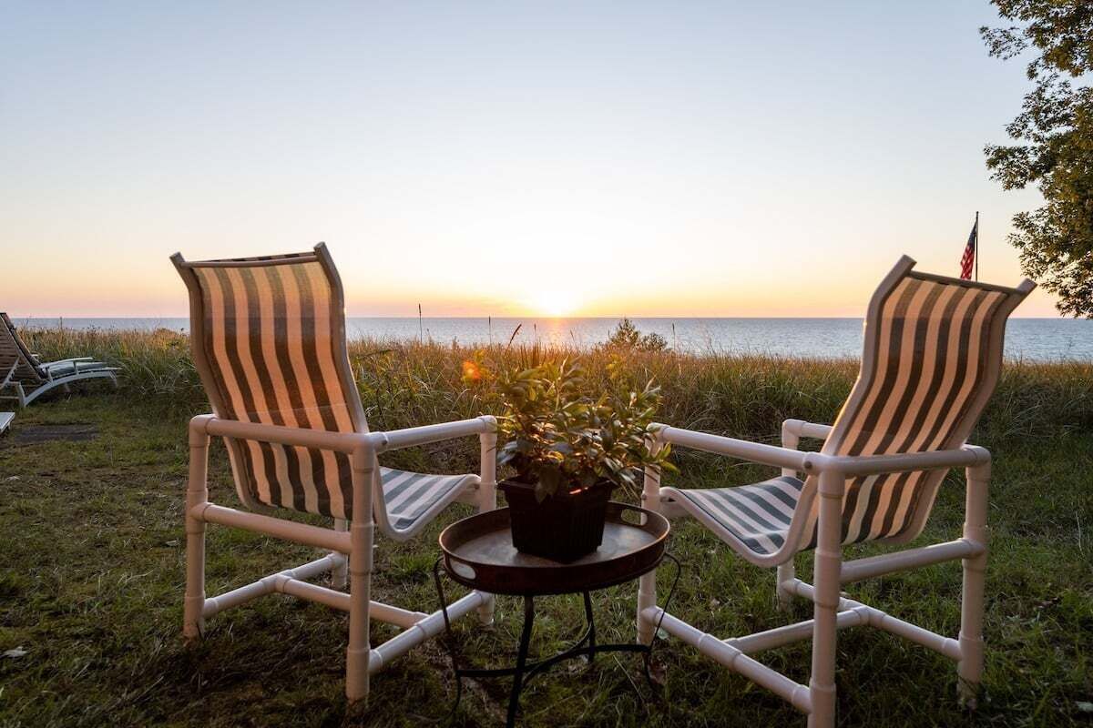 Two striped chairs facing a sunset over water, with a small table between them.