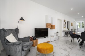 Una sala de estar moderna con un sofá gris, un otoman amarillo, un televisor de pantalla plana y una decoración de estilo minimalista.
