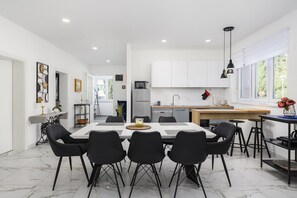 Una cocina moderna con armarios blancos, una isla central y un comedor con sillas negras.